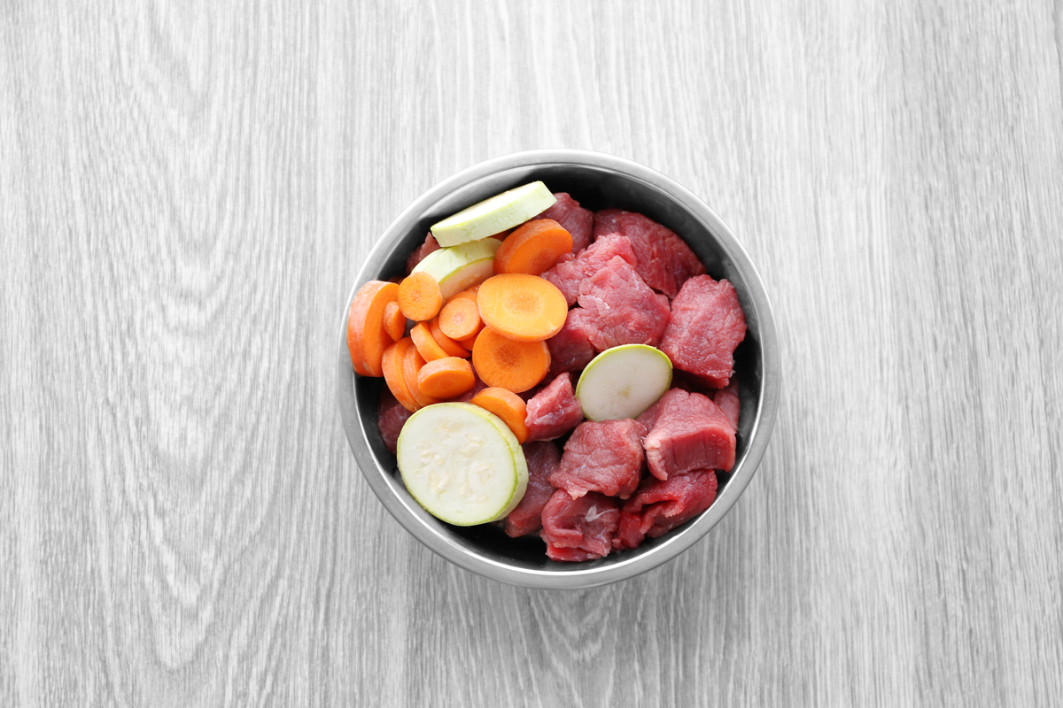 Silberner Napf gefüllt mit geschnittenem rohem Fleisch Karotten Gurken